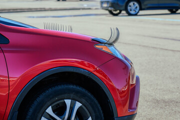 A red car in the mall parking lot has fake eyelashes above the headlights.  Funny accessory for an automobile driven by a woman.  