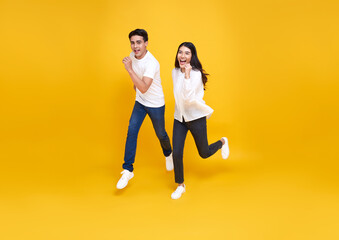 Happy energetic Asian couple running to shopping black friday low prices summer sale isolated on yellow studio background.