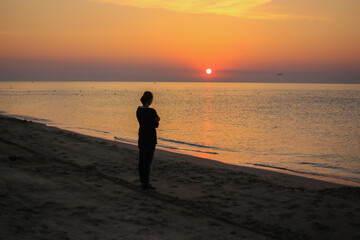 Fototapeta na wymiar Medium wide shot rear view of woman standing in surf on tropical beach watching sunrise