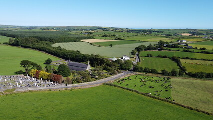 Fototapeta na wymiar Old church and cemetery among green farm fields, top view. Picturesque fields in the south of Ireland, landscape. Sacred Heart Roman Catholic Church. Green grass field under blue sky