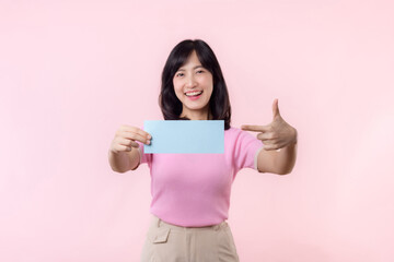 Portrait happy young woman model holding and showing blank space paper for advertisement information message poster with thumb up or point finger gesture isolated on pink pastel studio background.