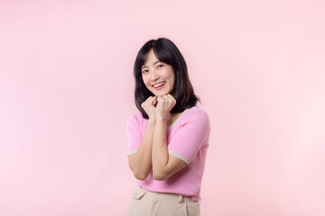 Fototapeta premium Adorable young happy asian woman model with shy emotion smiling expression cheerful positive attractive face and holding hand isolated on pink pastel studio background. Portrait beautiful cute lady.