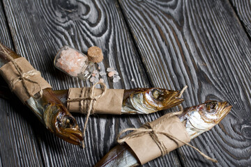 Putassu Cold smoked. The fish is wrapped with a strip of paper. Tied with linen twine. Lies on pine boards. An overturned jar of coarse salt. Close-up.