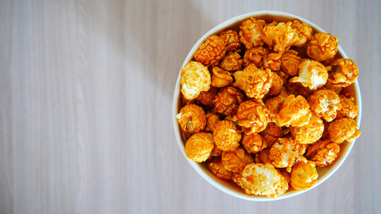 Top view of beautiful caramel popcorn in a cardboard cup on a wooden table close-up