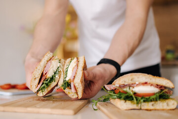 Handsome young man slice Italian sandwich and show what inside. Delicious lunch at home