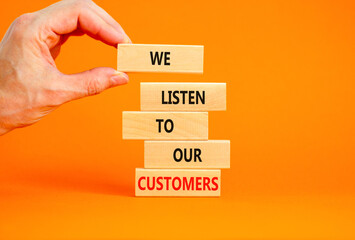 We listen to our customers symbol. Concept words We listen to our customers on wooden block. Beautiful orange background. Businessman hand. Business we listen to our customers concept. Copy space.