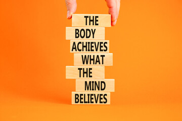 Mind and body symbol. Concept words The body achieves what the mind believes on wooden blocks. Beautiful orange background. Copy space. Businessman hand. Motivational mind and body concept.