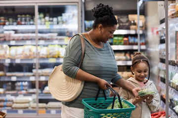 Portrait of mother shopping in supermarket with little daughter and buying vegetables