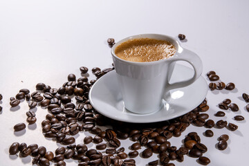 Espresso served in white cup and surrounding coffee beans on white background