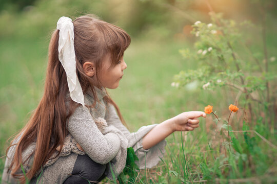 Little girl touch strokes orange flower in the park. Background summer green flowering on the lawn. Child playing on the spring nature outdoors.A rare flower of Trollius asiaticus listed in the red