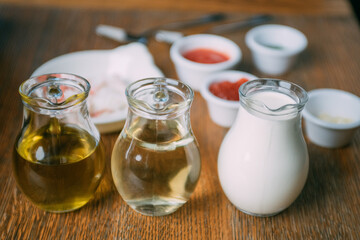 Ingredients for the sauce on the table: sunflower and olive oil, milk in jugs, bowls with sauces. Close-up