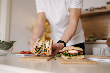 Handsome young man slice Italian sandwich and show what inside. Delicious lunch at home
