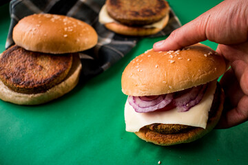 Some fresh burgers with vegetables and bread and hand taking one 