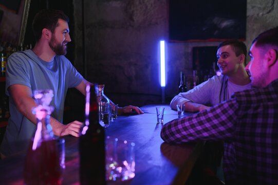 Attractive bartender is smiling and taking order of two men sitting at bar counter in pub