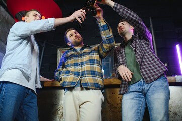 Fototapeta premium Old friends meeting. Happy young men in casual wear toasting with beer while sitting in beer pub together