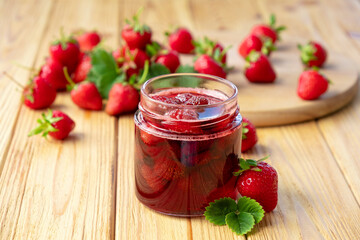 Strawberry jam in glass jar on wooden board with fresh strawberry fruit and green leaves on wooden background. Recipe of delicious homemade berry jam of strawberry full of vitamins and antioxidants.