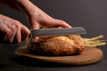 Whole grain bread put on kitchen wood plate with a chef holding knife for cut. Fresh bread on table...