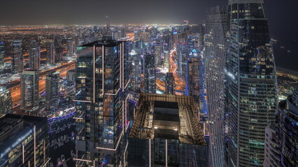 Panorama showing Dubai Marina and JLT district with traffic on highway between skyscrapers aerial night timelapse.