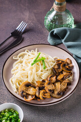 Udon noodles, fried champignons and greens on a plate on the table vertical view