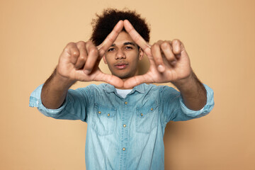 Portrait of handsome young man with dark skin and afro hair in blue denim shirt making and showing...