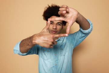 Young latin dark-skinned guy showing camera shape gesture with hands looking through at camera,...