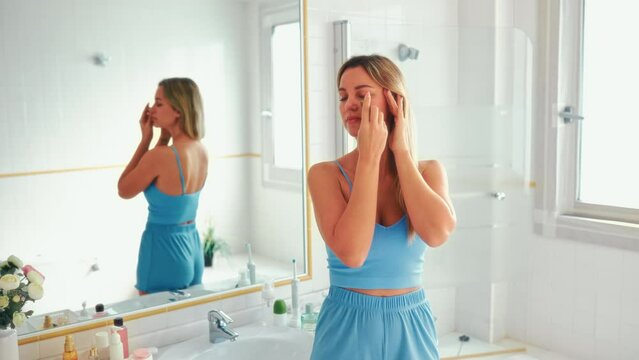 Beautiful woman in lingerie standing at the washbasin and mirror making face massage with gouache stone. Morning skin care routine. Cosmetology and spa procedures.
