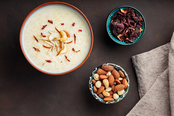 Rice kheer, nuts and dried hibiscus flowers on a dark background. Indian kheer rice pudding with nuts. Iftar muslim food concept. Top view