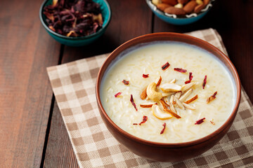 Rice pudding served in clay bowl. Indian rice kheer with nuts on a wooden background. Popular Ramadan dish. Top view