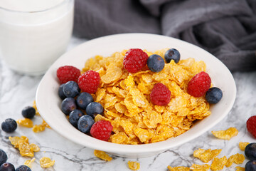 Tasty corn flakes with blueberries and raspberries in a black bowl with milk on marble table