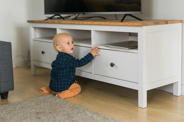 Toddler baby boy open cabinet drawer with his hand. Child explore what is in cabinet. Baby curiosity and child development stages