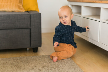 Toddler baby boy open cabinet drawer with his hand. Child explore what is in cabinet. Baby curiosity and child development stages