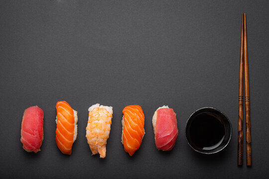 Traditional Japanese sushi top view with soy sauce and chopsticks on dark black minimal background. Sushi with salmon, tuna and shrimp, space for text