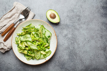 Healthy vegan green avocado salad bowl with sliced cucumbers, edamame beans, olive oil and herbs on...
