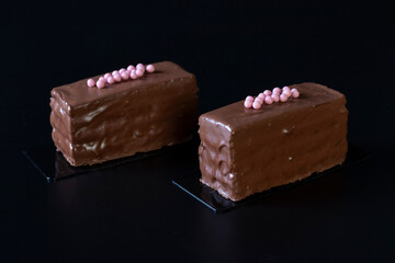 Two mousse chocolate desserts with chocolate cream and raspberry marmalade covered gourmet chocolate glaze on black background, Close up