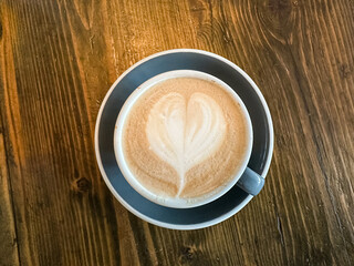 A cup of coffee latte on a wooden table. A mug of flat white coffee, latte, cappuccino on a wooden background. Coffee art. Heart flower swan shape latte art