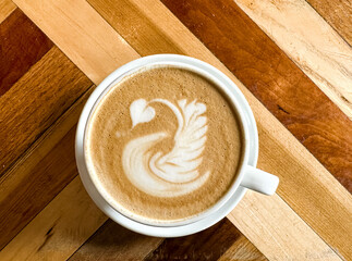 A cup of coffee latte on a wooden table. A mug of flat white coffee, latte, cappuccino on a wooden background. Coffee art. Heart flower swan shape latte art
