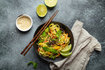 Asian vegetarian noodles with vegetables and lime in black rustic ceramic bowl, wooden chopsticks,...