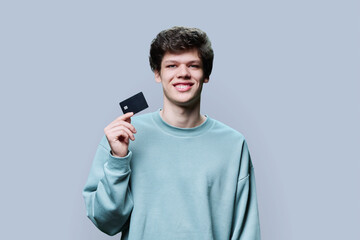 Naklejka premium Young handsome guy holding credit card in hands on grey background