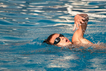 Boy child swimmer swim in outdoor swimming pool. Professional young athlete training front crawl technique. Water sports, training, competition, summer activities, healthy lifestyle, children's sport