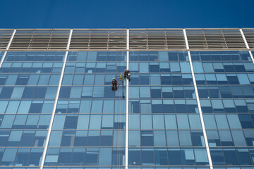 The Art of Cleaning Skyscraper: Glass building under blue sky and hanging glass cleaners