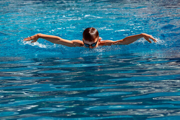 Boy child swimmer swims in swimming pool with butterfly style. Water sports, training, competition, activities, learn to swim school classes for children