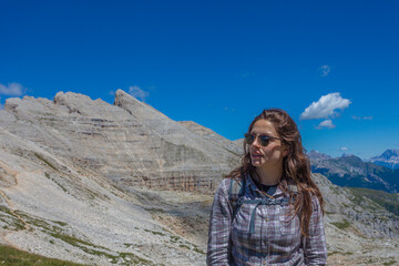Naklejka premium Portrait of young woman with sunglasses and long hair. Scenic landscape on the nature, Mount Latemar, Trentino, Italy. Traveling photography and outdoor sport activity concept