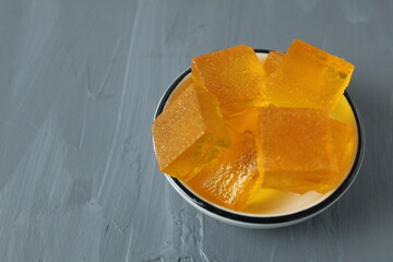 orange marmalade orange in a bowl plate on a gray background with a mixture for text. healthy dessert on agar. Orange cubes pieces of marmalade