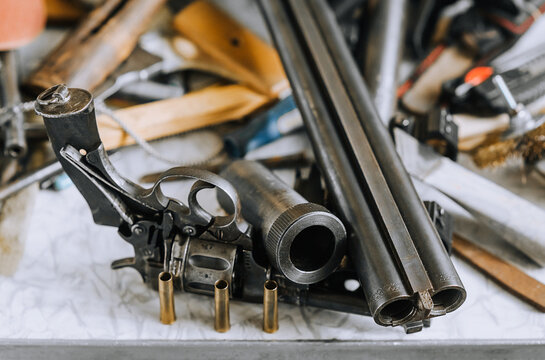 Old weapons of various calibers, a rifle, a metal revolver with cartridges, barrels, parts and accessories, ammunition lie on the table. Closeup photography, firearms concept, collection.