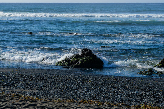 Waves crashing into a rock in a peaceful beach with black sand in Las Galletas, coast of Tenerife