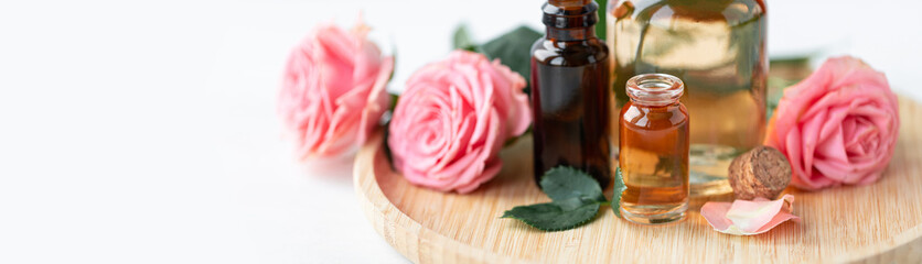 Aromatherapy. Pure organic essential rose oil concept. Elixir with plant based floral herbal ingredients. Pink flowers extract. Spa atmosphere with candle, towel. White background. Banner copy space