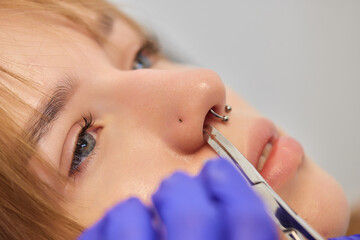 Young woman doing piercing nose ring at beauty studio salon.