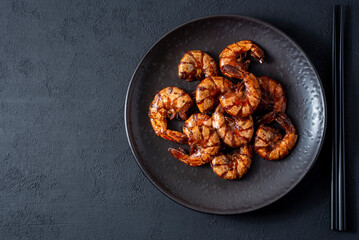 Grilled fried shrimp on a black plate dark background top view