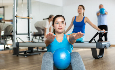 Fototapeta na wymiar Group of young elderly people in sportswear exercising Pilates with mini balls while lying on mats in rehabilitation center