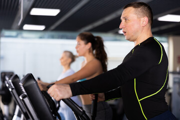 Fototapeta na wymiar Portrait of motivated sporty adult man doing cardio training, exercising on elliptical trainer in gym